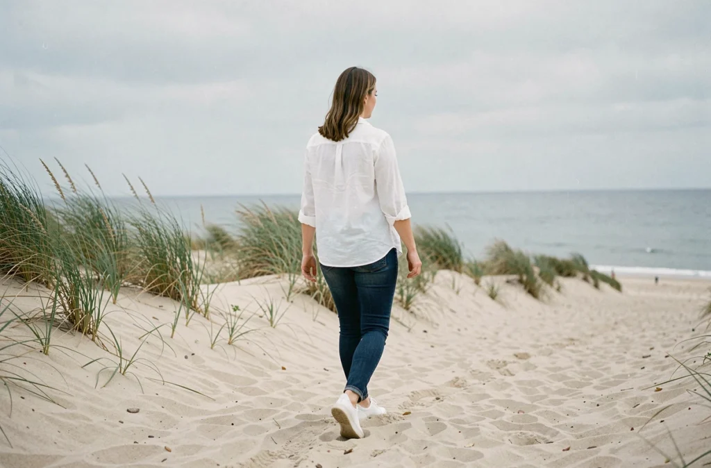 Femme enceinte de profil marchant sur un sentier côtier en bord de mer, tenue décontractée en lin blanc, ambiance apaisante